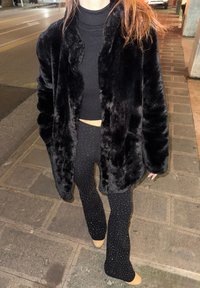 Svart kunstpelsjakke med rundet krage, kombinert med en svart croppet ribbestrikket topp og vide leggings med spredte sølvstift.