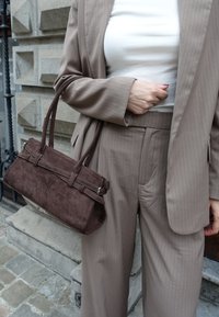 Pruun sametist käekott kahe ülemise sangaga, millel on ristkülikukujuline vorm, õmmeldud detailid ja klambri sulgemisviis, koos beeži triibulise ülikonnaga.