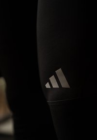 Leggings atletici neri con logo Adidas riflettente sulla coscia, con texture liscia e design aderente.