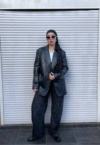 Czarny skórzany blezer na białej koszuli, zestawiony z czarnymi jeansami o szerokich nogawkach z srebrnymi zdobieniami oraz czarnymi butami. Uzupełniony okularami przeciwsłonecznymi i biżuterią.