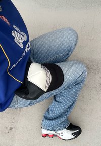 Sininen paita valkoisella kuviolla, vaaleansiniset kuvioidut farkut, musta-valkoinen pesäpallohattu graafisella kuvastolla ja hopeiset Nike-tennarit punaisilla yksityiskohdilla.