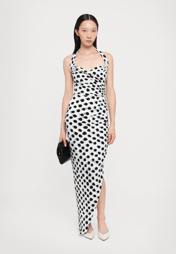 Musta-valkoinen pilkullinen mekko, jossa on halterneck-olkaimet, tiukka istuvuus, sivuaukko ja sileä kangas. Yhdistetty mustan laukun ja valkoisten korkokenkien kanssa.