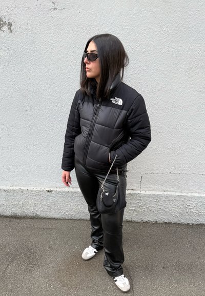 Chaquetón negro acolchado con diseño de cuadros, pantalones negros de cuero sintético, bolso negro pequeño con cadena, zapatillas blancas y gafas de sol oscuras.