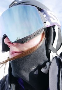 Schwarzer Fleecepulli-Schlauchschal mit Buff-Logo, violette Skibrille mit verspiegelten Gläsern und schwarzer Helm. Mit Riemen und angebrachtem Clip.