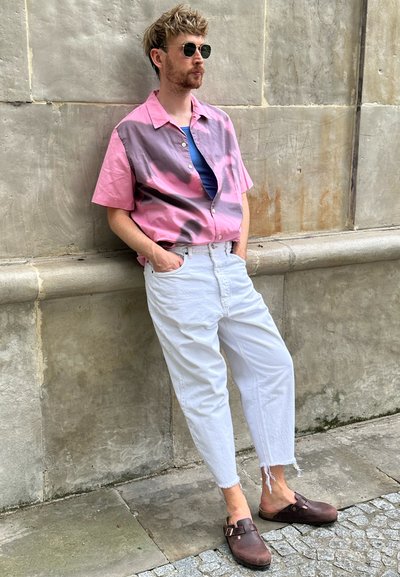 Camisa de manga corta en degradado de rosa a gris, camiseta interior azul, jeans blancos de corte holgado y zapatos marrones sin cordones con detalle de hebilla.