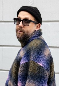 Fleecová bunda s farebným blokovým dizajnom v modrých, hnedom a fialových tónoch. Vysoký golier, zapínanie na zips a mäkká, textúrovaná látka.