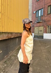 Lys farget, ermeløs topp med samlet kant, sammen med mørke jeans. En camouflage-mønstret caps fullfører antrekket.