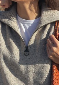 Svetlo sivi zip-up pulover z visokim ovratnikom, teksturirano pletenje in pisane pike. Zadrga ima krožno vlečko, v kompletu z tkano oranžno torbico.