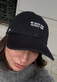 Black cotton baseball cap featuring embroidered white text that reads "my dog is my child." It has a curved brim and an adjustable strap at the back.