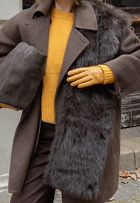 Barna gyapjúkabát műszőrme szegéllyel, mustár színű kötött pulóver, szürke velúr táska és narancssárga bőr kesztyű. Texturált és rétegzett design elemek.