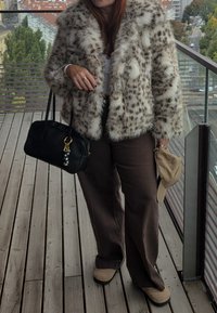 Faux fur jacket with spotted pattern, brown wide-leg pants, black handbag with gold accents, and beige shoes. Wooden floor in background.