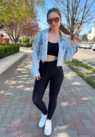 Chaqueta de mezclilla recortada de color azul claro sobre un top corto negro ajustado y leggins negros de cintura alta, combinada con zapatillas blancas en un camino de ladrillos.