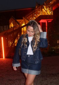 Jeansjacke mit einem hellen Waschung, mit kontrastierenden Manschetten, kombiniert mit einem passenden Jeansrock. Darunter ein weißes Top, in der Dämmerung.