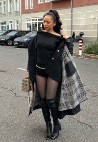 Czarny top na jedno ramię z prążkowanej dzianiny, szorty pokryte cekinami i czarne skórzane buty za kolano. Szary płaszcz z podszewką w kratę, czarną zewnętrzną warstwą i złotą torebką.