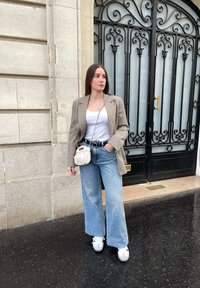 Beige kavaj med rutmönster, vit linne, ljusblå vida jeans, vita sneakers och en liten krämfärgad axelremsväska. Svart utsirad dörr i bakgrunden.
