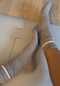 Grijze geribbelde sokken met witte strepen aan de boord, getoond op een gestructureerd oppervlak. De positie van de voeten creëert een ontspannen uitstraling.