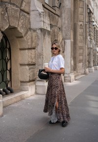 Jupe maxi imprimée léopard avec fentes sur les côtés, accompagnée d'un t-shirt blanc. Les accessoires incluent des lunettes de soleil noires et un sac noir matelassé.