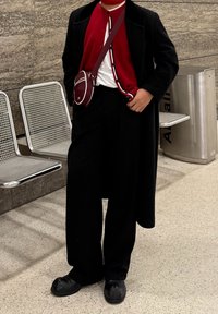 Manteau noir, cardigan rouge avec des rayures blanches, t-shirt blanc, pantalon large noir et chaussures noires. Petit sac à bandoulière rouge.