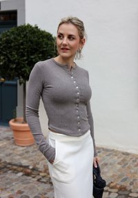 Grijze lange mouwen cardigan met knopen, geribbelde textuur, cropped ontwerp, gecombineerd met een witte rok met zakken, voor een neutrale achtergrond.