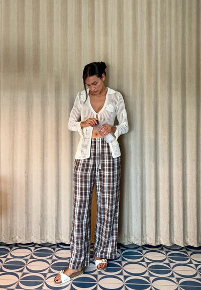 Cárdigan blanco de punto con cuello y botones, combinado con pantalones de pierna ancha en cuadros marrones y blancos. Sandalias de color claro con tiras.
