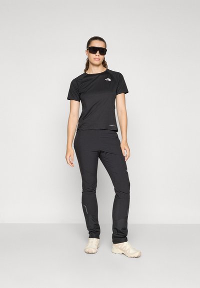Camisa y pantalones deportivos negros hechos de tejido que absorbe la humedad. Los pantalones cuentan con bolsillos con cremallera y acentos reflectantes. El modelo lleva gafas de sol.