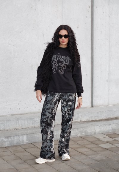 Sudadera negra con estampado gráfico, combinada con pantalones de flores en negro y gris. Accesorios incluyen gafas de sol y un chaleco negro con textura.