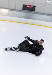 En person iført sort læder slapper af på en skøjtebane og holder en hvid tekop. De har sorte og hvide skøjter på og lilla hår.