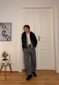Veste en cuir noire avec doublure grise contrastante, t-shirt blanc, pantalon large gris et chaussures noires. Inclut des plantes et des bougies sur une table en verre.