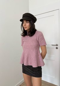 Haut rose pâle à manches courtes avec un ourlet évasé, associé à une mini-jupe noire. Le modèle porte une casquette foncée à finition texturée.