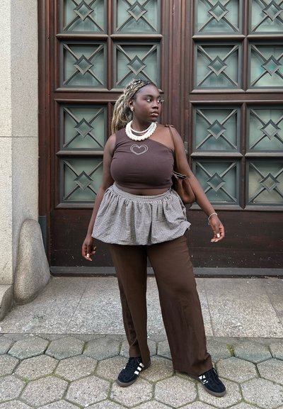 Top de tirantes marrón con detalle de corazón, peplum a cuadros, pantalones anchos marrones y zapatillas negras. Accesorios con un collar de perlas y un bolso marrón.