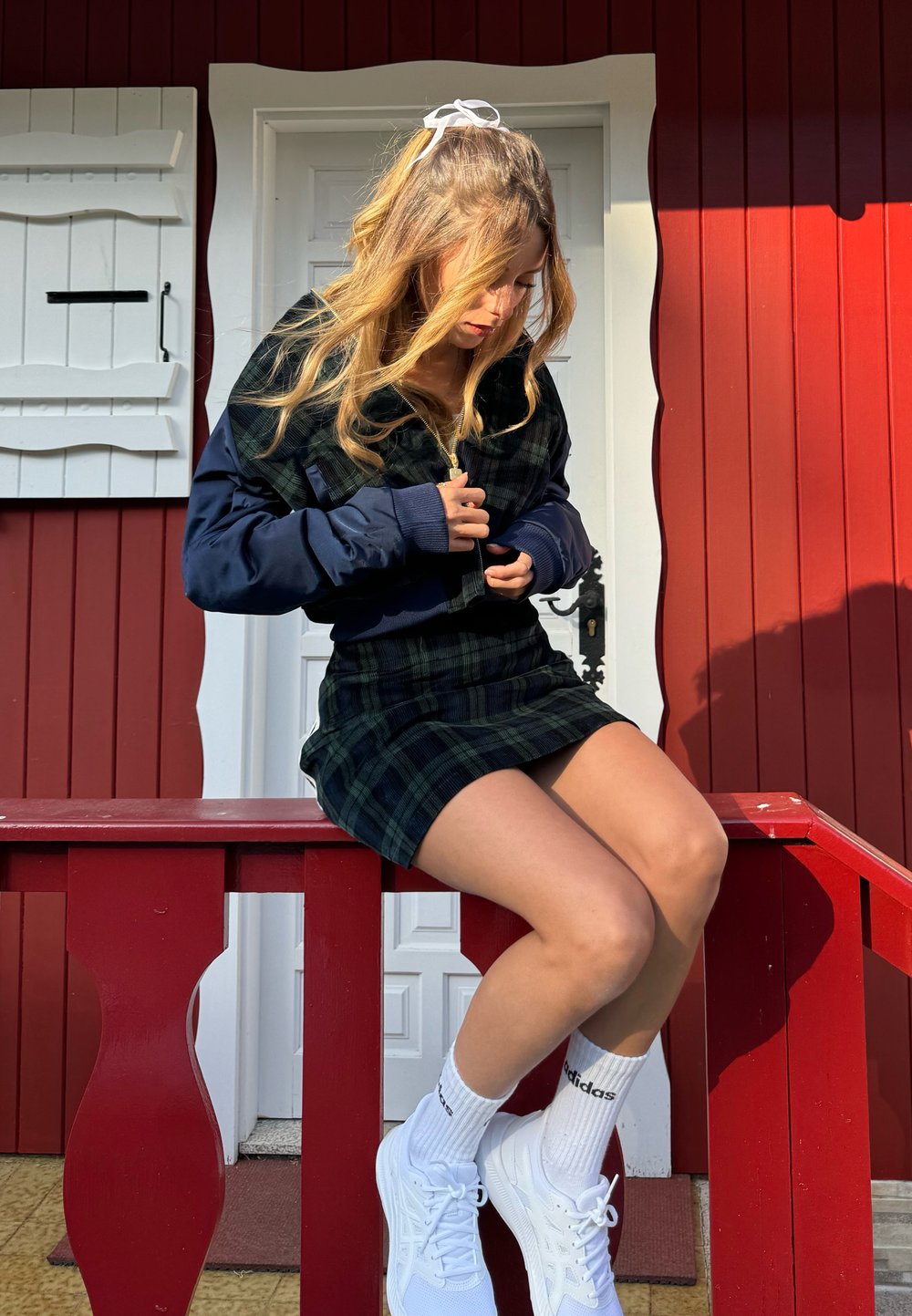 Πράσινο και ναυτικό καρό cropped μπουφάν με φερμουάρ, συνδυασμένο με μία ταιριαστή εφαρμοστή φούστα. Λευκά sneakers και επώνυμες κάλτσες ολοκληρώνουν την εμφάνιση.