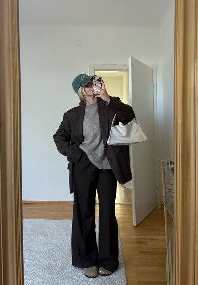 Blazer de cuadros marrón de gran tamaño, suéter gris, pantalones de pierna ancha negros, gorra verde y bolso blanco. Calzado marrón con tachuelas. Reflejo en el espejo.