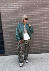 Πράσινο σατέν bomber jacket, λευκή μπλούζα, λεοπάρ φαρδιά παντελόνια και λευκά αθλητικά παπούτσια, αξεσουάρ με μαύρη τσάντα και ηλιόβλεφα.