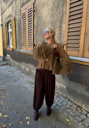 Brown pleated top with ruffled sleeves, matched with loose dark brown trousers. Accessorised with heeled ankle boots and a textured brown handbag.