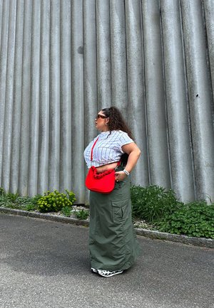 Bolso rojo con diseño de volantes, camiseta corta blanca con rayas negras, falda larga verde de cargo, zapatillas negras y blancas, gafas de sol.