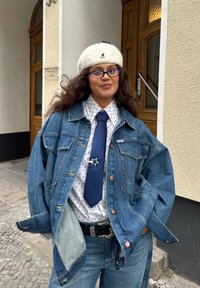Denimjakett, valge särk siniste täppidega, sinine lips tähe kinnitusega ja hall beret. Looduslik lõige ja kihilised tekstuurid, aksessueeritud rihmaga.