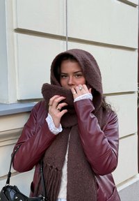 Écharpe en fausse fourrure marron et pull assorti sous une veste en cuir bordeaux. Un petit sac à main noir et des bagues argentées accentuent le look.