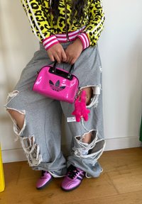 Melna un rozā Adidas rokas soma ar diviem rokturiem, savienota ar pelēkiem pārāk liela izmēra izsistajiem treniņbiksēm un spīdīgām rozā kedām.