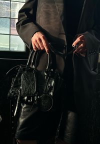 Μαύρη δερμάτινη τσάντα χειρός με πολλούς χώρους αποθήκευσης, υφή στην επιφάνεια, κοντά χερούλια και διακοσμητικά αξεσουάρ. Γυαλιστερή φινίρισμα με στρογγυλό αξεσουάρ.