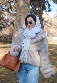 Bézs műszőrméből készült dzseki, nagy ujjakkal, világosszürke sállal és barna bőr kézitáskával párosítva, lágy textúrával.