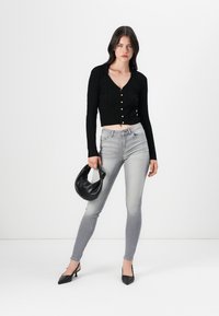 Schwarzes geripptes Croptop mit goldenen Knöpfen, hellgraue Skinny Jeans, eine schwarze Handtasche und schwarze spitze High Heels. Minimalistisches Design.