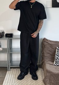 Svart oversize t-shirt och vida byxor i mjukt tyg, kombinerat med svarta snörstövlar; minimalistisk design utan mönster.