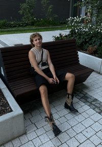 Μαύρες και μπεζ ankle μποoots, λεία υφή, μυτερή μύτη, ελαστικές λεπτομέρειες. Ανοιχτό μπεζ αμάνικο τοπ, μαύρες σορτς, καθισμένη σε ξύλινο πάγκο.