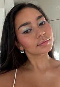 Nærbilde av en person med langt, mørkt hår. Har pastellblå og sølvøyenskygge, glatt hud og en stor, rektangulær sølvøredob.