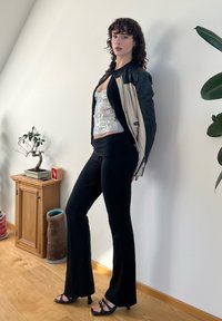 Pantalons noirs évasés, haut ajusté argent métallique et une veste bicolore noire et crème. La tenue est complétée par des talons noirs à lanières.