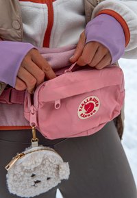 Sac Fjällräven Kånken rose avec une fermeture à rabat et un patch logo, attaché à une ceinture grise ; adorable pochette ronde zippée en forme de mouton.