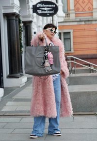 Saco tote de couro cinza com alças de ombro, apresentando chaveiros peludos. Usado com um casaco de pelúcia rosa e jeans de perna larga azul claro.