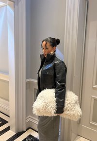 Sort læderjakke med høj krave, grå kjole og en fluffy hvid tekstureret taske, sat op mod lysegrå vægge og mønstret gulv.