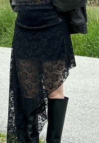Jupe en dentelle noire avec un ourlet asymétrique, design superposé, texture semi-transparente, associée à des bottes noires élégantes jusqu'au genou.