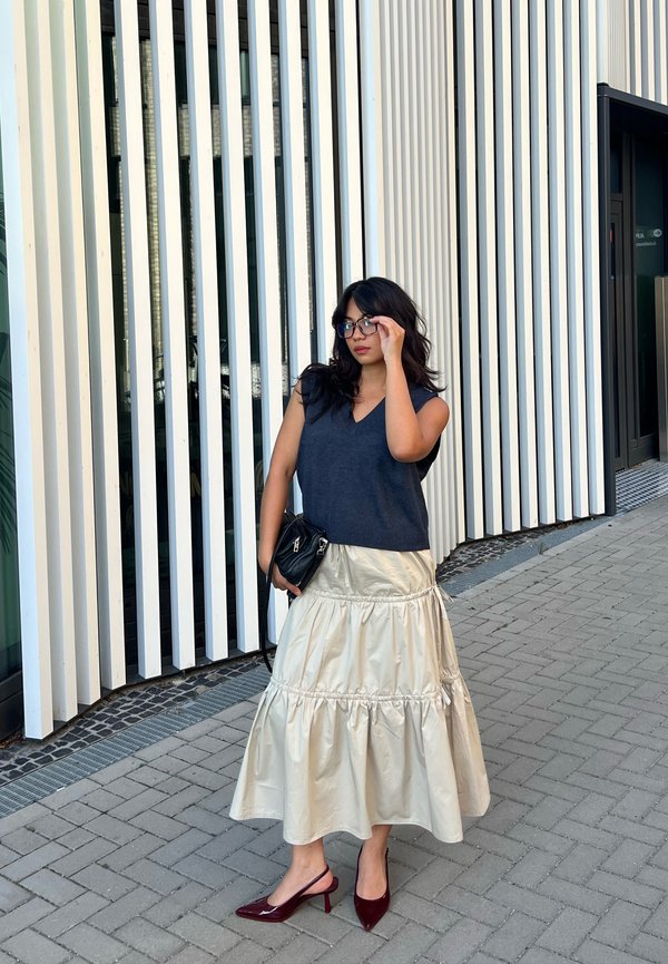 Top senza maniche blu navy abbinato a una gonna a strati in satin crema, accessoriato con una borsa nera e scarpe con tacco rosse, posto su uno sfondo a righe.